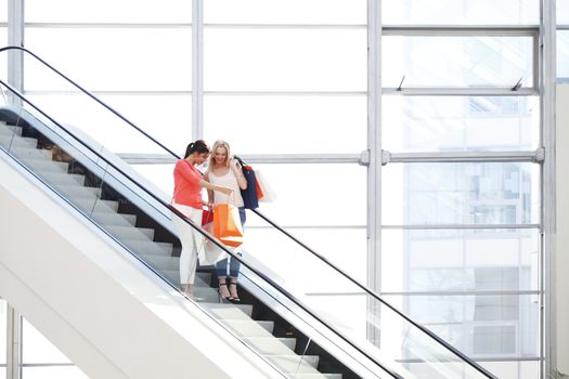 Young beautiful happy women on escalator of shopping mall