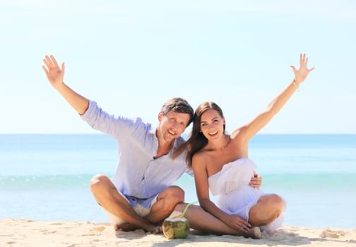 Cheerful couple sitting on beach and waving hands 