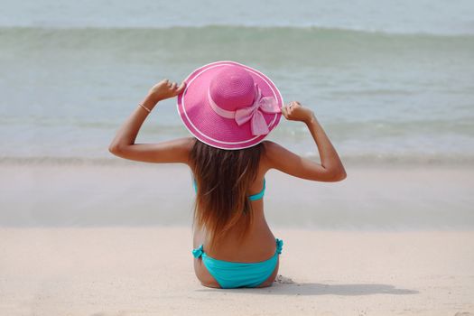 Woman in big hat sitting on beach by the sea