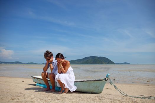 Sad couple sitting on old boat on tropical beach