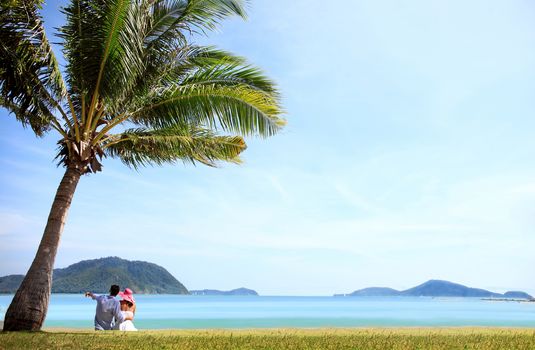 Happy young caucasian couple sitting under palm near the sea 