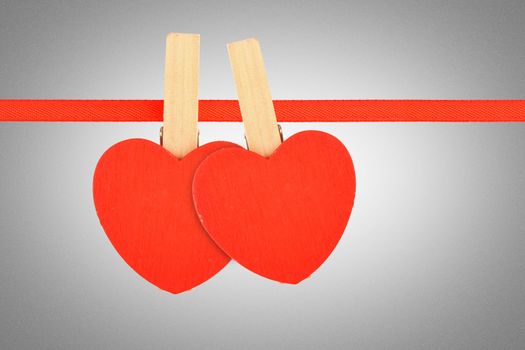 Valentine day template, two red wooden hearts with clothes pins on textile ribbon over grayscale grain noise gradient