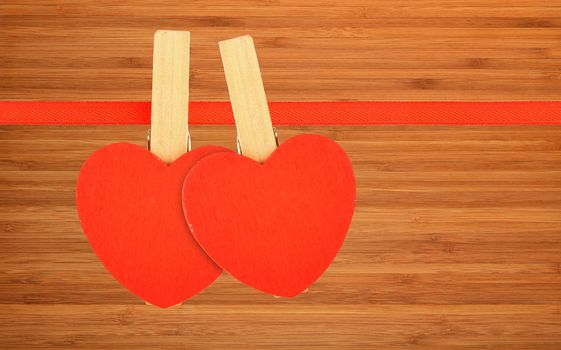 Valentine day template, two red wooden hearts with clothes pins on textile ribbon over bamboo wood board surface