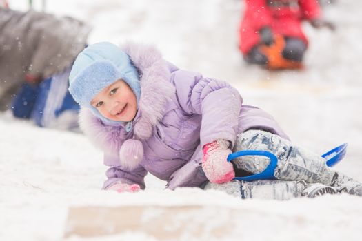 Five-year girl riding winter on a snowy hill surrounded by other children