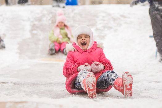 Seven year old girl riding a ledyankah winter on a snowy hill surrounded by other children