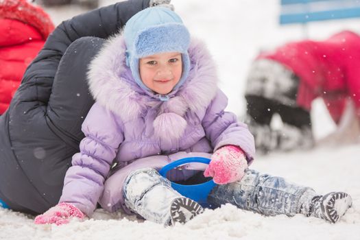 Five-year girl riding winter on a snowy hill surrounded by other children