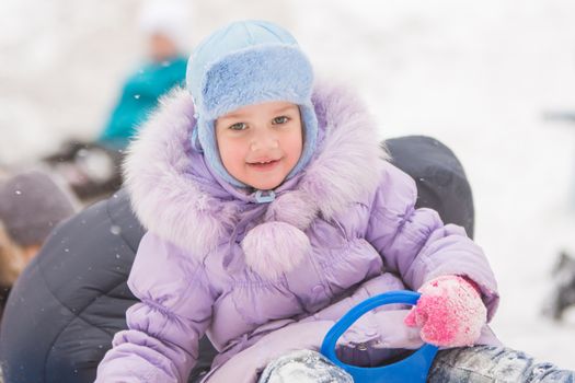 Five-year girl riding winter on a snowy hill surrounded by other children
