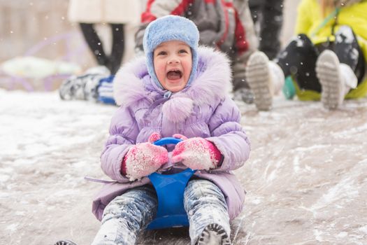 Five-year girl riding winter on a snowy hill surrounded by other children