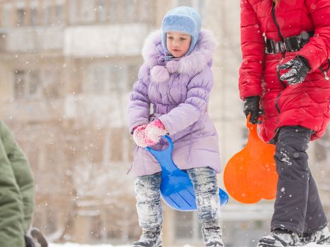 Five-year girl riding winter on a snowy hill surrounded by other children