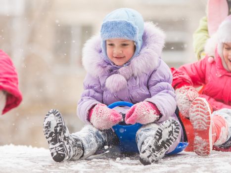 Two girls in the winter ride on a snowy hill surrounded by other children