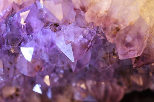 Purple and white natural amethyst geode background pattern glitters in the light.