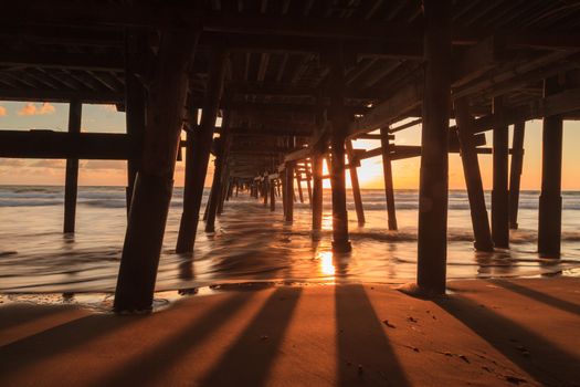 Under the San Clemente pier on the beach at sunset in the fall in Southern California, United States.