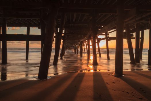 Under the San Clemente pier on the beach at sunset in the fall in Southern California, United States.