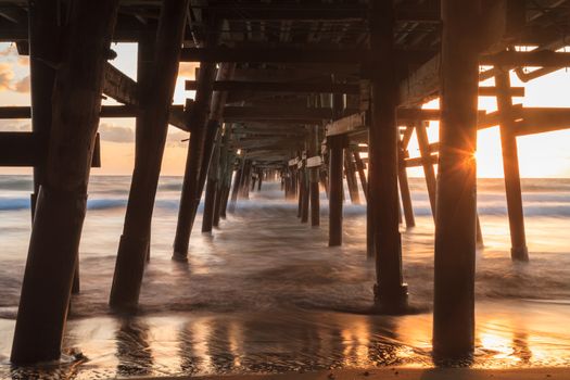 Under the San Clemente pier on the beach at sunset in the fall in Southern California, United States.