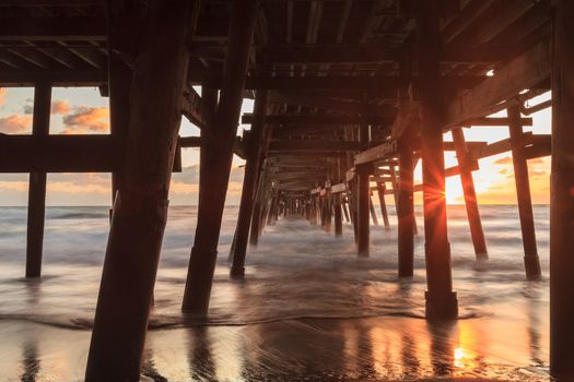 Under the San Clemente pier on the beach at sunset in the fall in Southern California, United States.