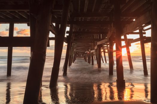 Under the San Clemente pier on the beach at sunset in the fall in Southern California, United States.