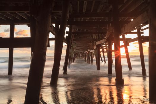 Under the San Clemente pier on the beach at sunset in the fall in Southern California, United States.