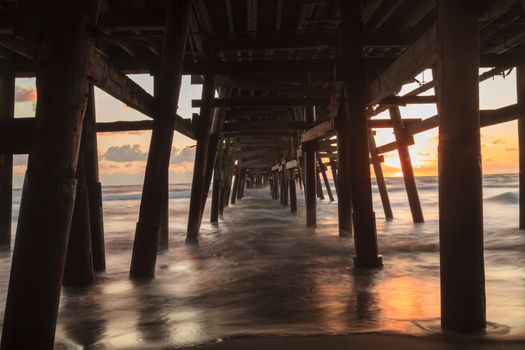 Under the San Clemente pier on the beach at sunset in the fall in Southern California, United States.