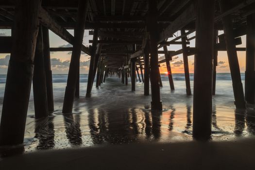 Under the San Clemente pier on the beach at sunset in the fall in Southern California, United States.