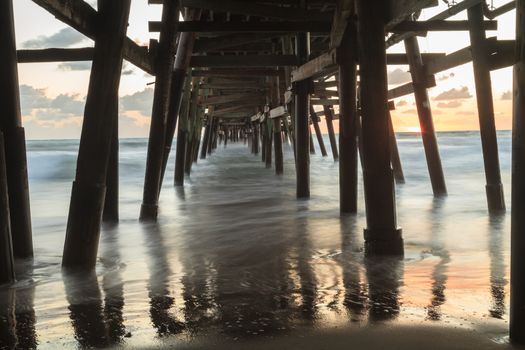 Under the San Clemente pier on the beach at sunset in the fall in Southern California, United States.