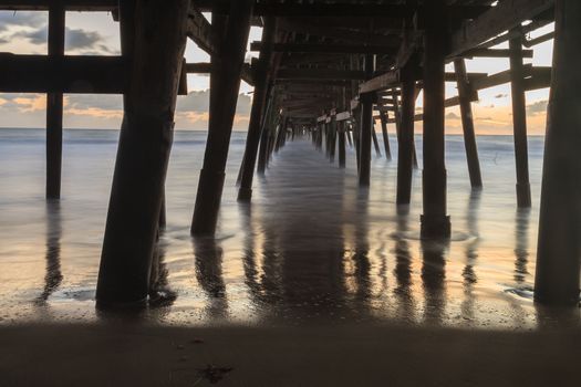 Under the San Clemente pier on the beach at sunset in the fall in Southern California, United States.