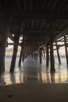 Under the San Clemente pier on the beach at sunset in the fall in Southern California, United States.