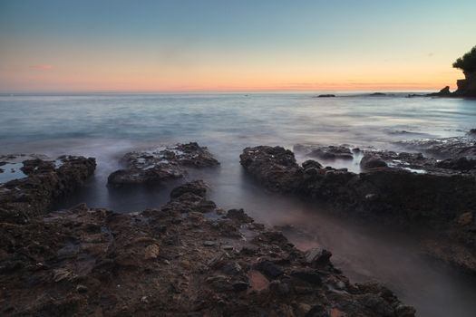 Long exposure of sunset over rocks, giving a mist like effect over ocean in Laguna Beach, California