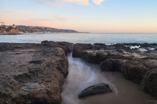 Long exposure of sunset over rocks, giving a mist like effect over ocean in Laguna Beach, California