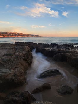 Long exposure of sunset over rocks, giving a mist like effect over ocean in Laguna Beach, California