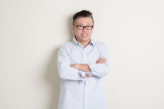 Portrait of happy single mature 50s Asian man in casual business smiling, standing over plain background with shadow.