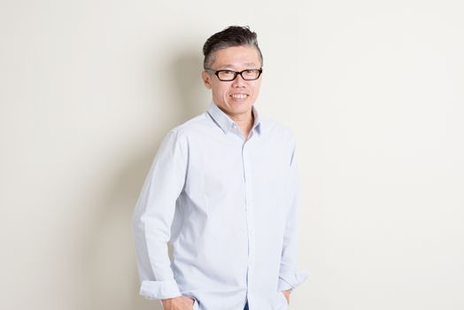 Portrait of confident single mature 50s Asian man in casual business arms crossed and smiling, standing over plain background with shadow. Chinese male people.