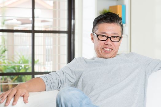 Portrait of happy mature 50s Asian man sitting at home. Senior Chinese male relaxed and seated on sofa indoor.