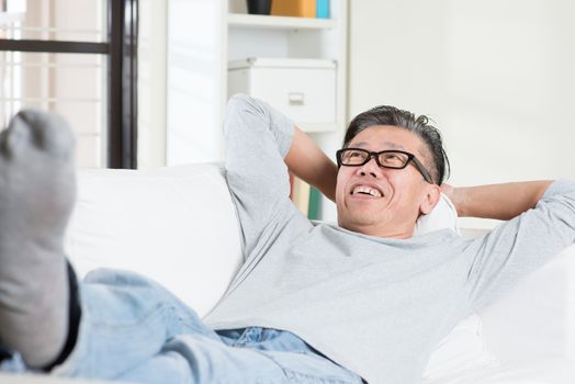 Mature 50s Asian man daydreaming and rest at home. Senior Chinese male relaxed and lying on sofa indoor. 