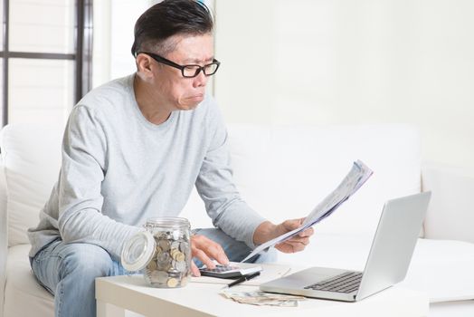 Worried 50s mature Asian man looking at the bills. Saving, retirement, retirees financial planning concept.