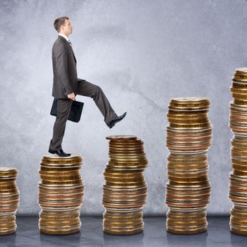 Businessman walking on stack of coins on grey background