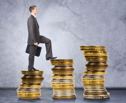 Businessman walking on stack of coins on grey background