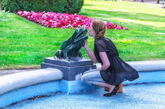 Young woman kissing in a fountain frog sculpture.