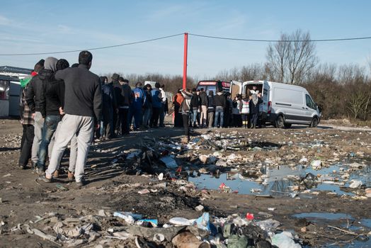 FRANCE, Calais: People stand in line on January 25, 2016, in the migrant shantytown on the outskirts of Calais known as the Jungle, where thousands are trying to make their way across the English Channel.A prefectoral decree posted on January 19, 2016, gave people 24 hours to leave the premises of a 100 metre wide strip of land in the jungle, where several small food businesses and restaurants had been set up, before its evacuation and destruction.