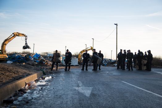 FRANCE, Calais: Policemen stand as bulldozers demolish part of the Jungle in Calais, northern France on January 25, 2016.