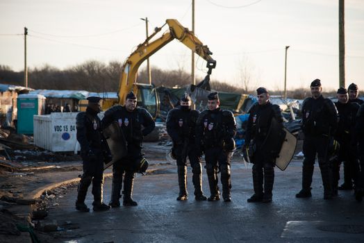 FRANCE, Calais: Policemen stand as bulldozers demolish part of the Jungle in Calais, northern France on January 25, 2016.