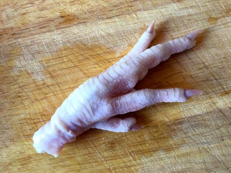 One raw chicken foot on a cutting board.