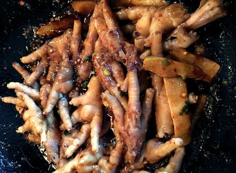 Spicy chicken feet frying in a wok.