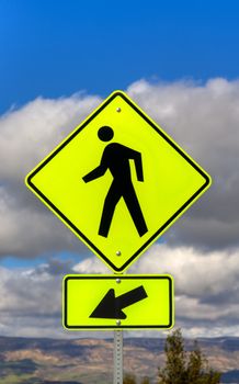 Yellow crosswalk sign with human icon and arrow pointing left.