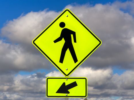 Yellow crosswalk sign with human icon and arrow pointing left.