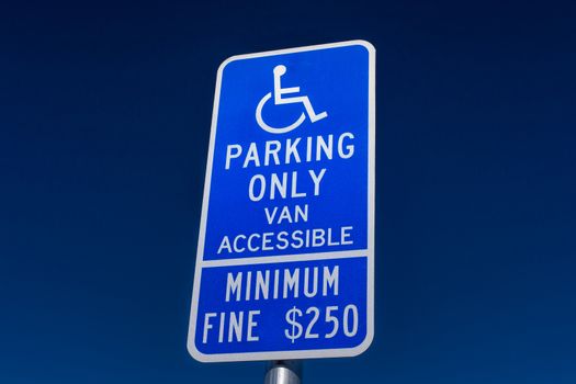 Handicapped parking sign with white lettering on blue backdrop.