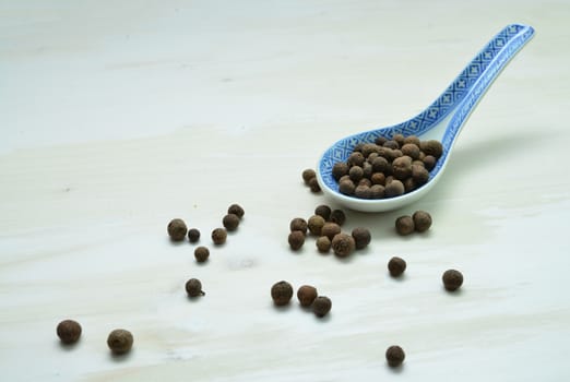 allspice seeds spoon over white wood background