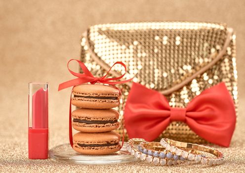 Macarons french dessert, Luxury shiny glamor fashion handbag clutch, lipstick, bracelets, red bow. Vintage retro romantic style. Unusual creative art greeting card, gold party background, bokeh