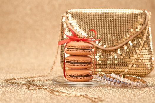 Macarons french dessert, Luxury shiny glamor fashion handbag clutch, bracelets, red ribbon. Vintage retro romantic style. Unusual creative art greeting card, gold party background, bokeh