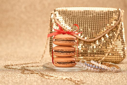 Macarons french dessert, Luxury shiny glamor fashion handbag clutch, bracelets, red ribbon. Vintage retro romantic style. Unusual creative art greeting card, gold party background, bokeh