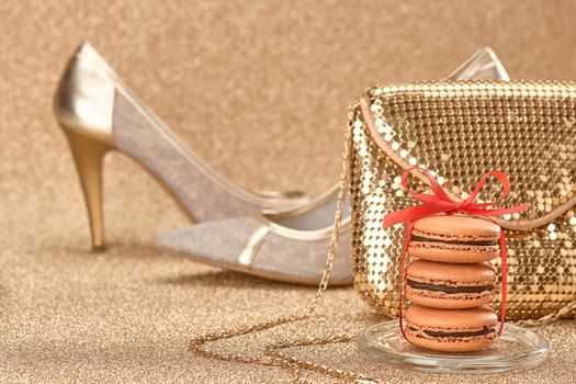 Macarons french dessert, Luxury shiny shoes high heels, glamor fashion handbag clutch, red ribbon. Vintage retro romantic style. Unusual creative art greeting card, gold party background, bokeh